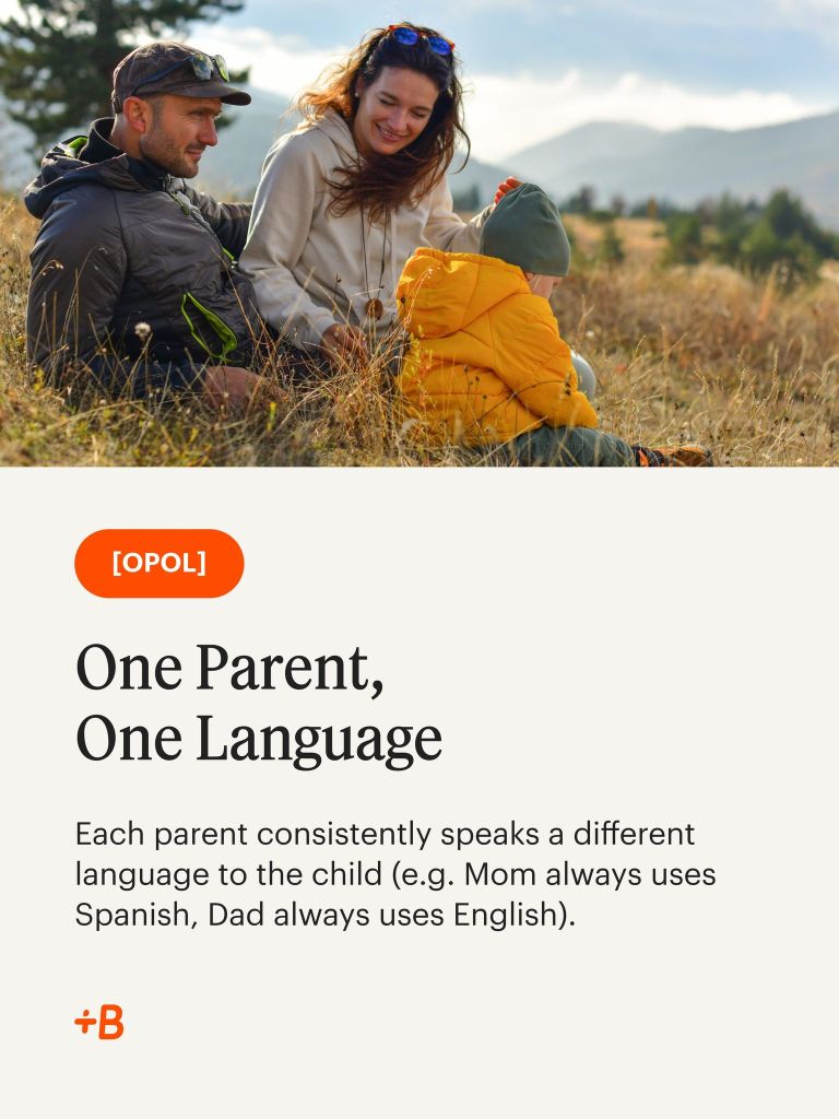 A mother, father, and young child sit together on a grassy hillside, smiling and enjoying each other's company. The child is wearing a bright orange jacket, while the parents are dressed casually for the outdoors. In the background, mountains and trees can be seen under a cloudy sky.