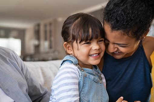 A smiling child sitting on the lap of an adult, both showing affection in a cozy indoor setting.