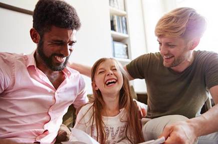 Two men and a young girl are sitting together, laughing and enjoying a moment of joy in a cozy home setting.