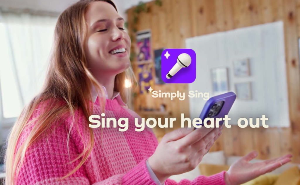 A young woman in a pink sweater joyfully singing while holding a phone, with the 'Simply Sing' logo and caption 'Sing your heart out' in the foreground.